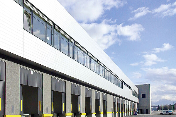 Schlüsselfertiger Industriebau für die Logistik mit eingebauten Kühlraum / Tiefkühlraum der Plattenhardt und Wirth GmbH. Die Verladezone mit Anfahrrampen sind in der Front eingebaut vor Wolken am Himmel.