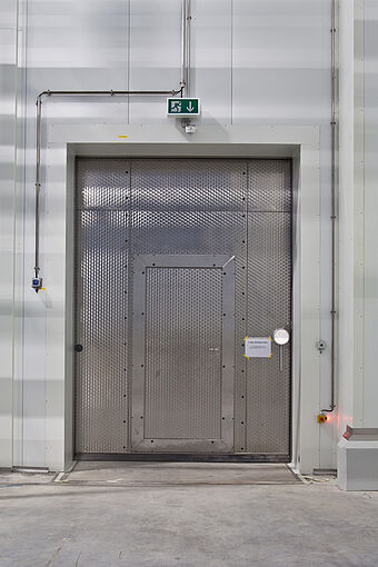 Edelstahl Kühlraumtüre in einem Kühlraum mit eingebauter betriebsraumdrehtüre für den Durchgang eines Rettungsweges. Hersteller für den Kühlraumbau ist die Firma Plattenhardt+Wirth. 
