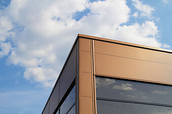 Die Ecke einer Paneelfassade eines schlüsselfertigen Bauvorhabens vor blauem Himmel mit Wolken.
